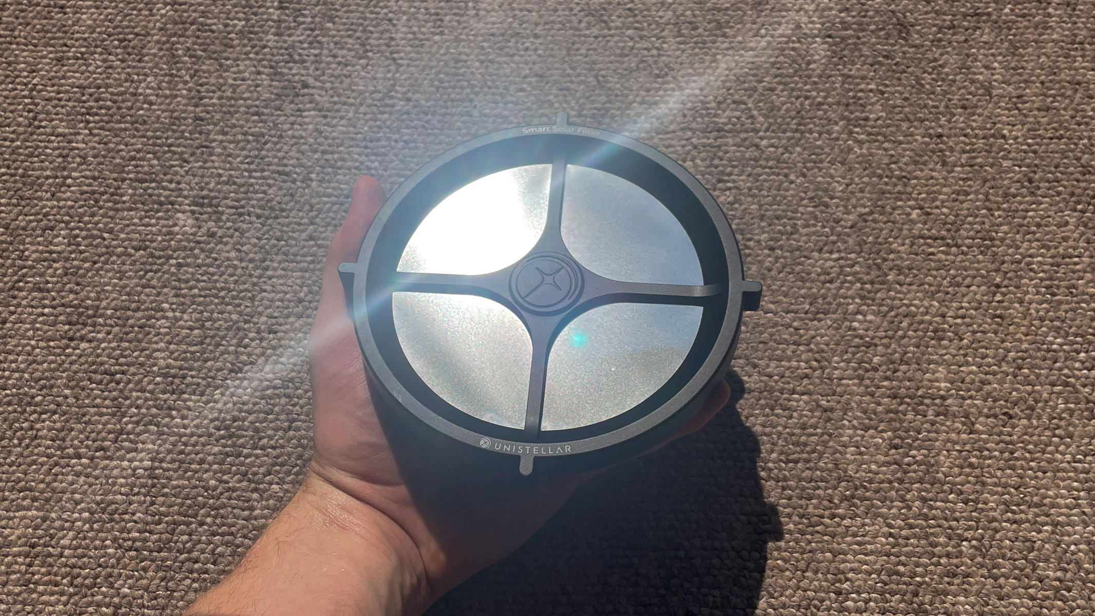 A hand holding the Unistellar eVscope 2 solar filter shining in the sunlight.