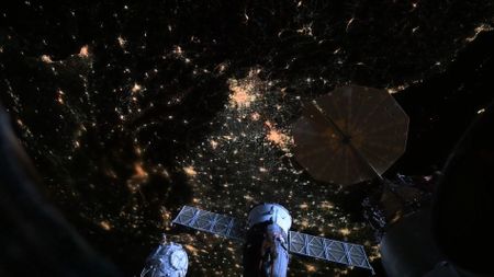 City lights are visible on the night side of Earth between the solar panels of docked spacecraft in a picture captured from the International Space Station.