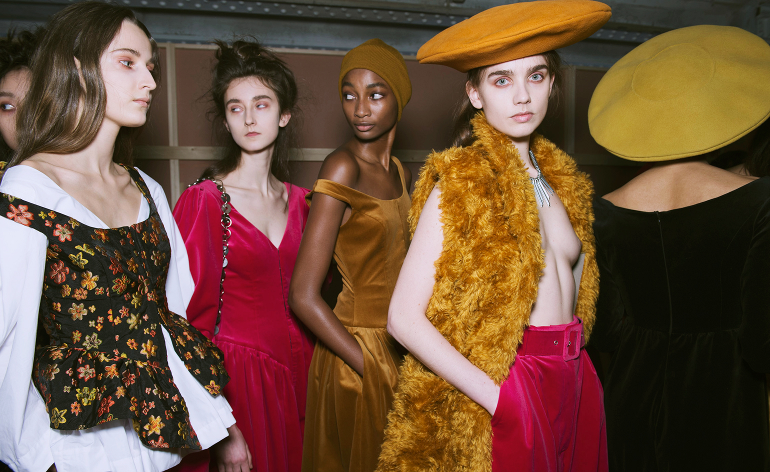 Model wears a pink velvet dress, whilst another in a layered shirt dress, and another in a yellow furry gilet