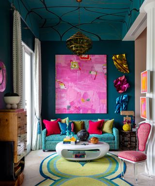maximalist living room with teal walls and ceiling, bright pink artwork and colorful sofa and cushions