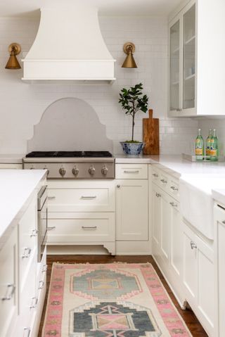 white kitchen with colorful rug on floor and traditional cooker hood above stove