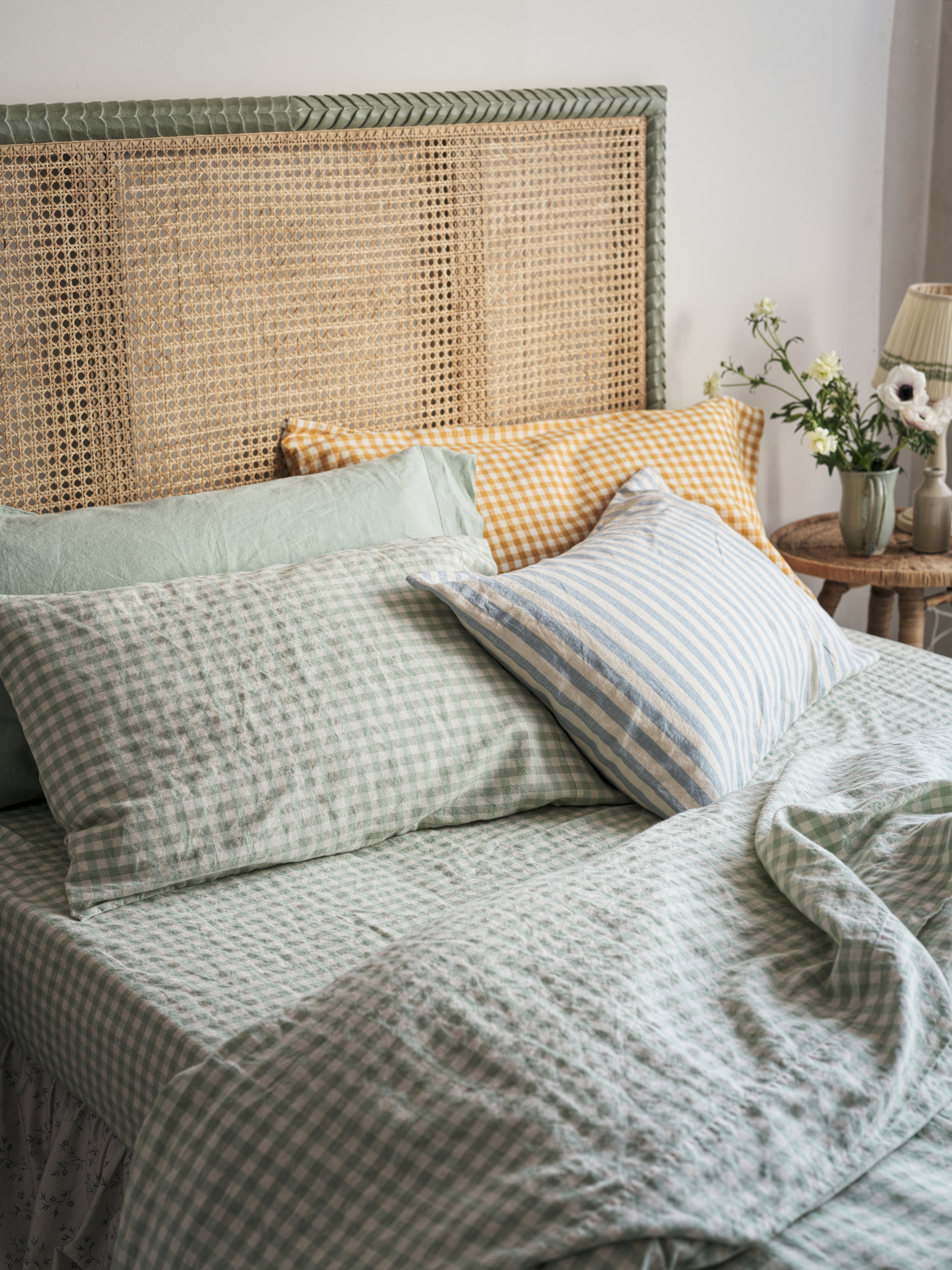 A bed with a cane headboard and green and white checkered bedding