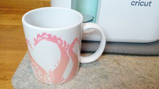A Cricut Mug Press designer mug sat on a table with a Mug Press machine