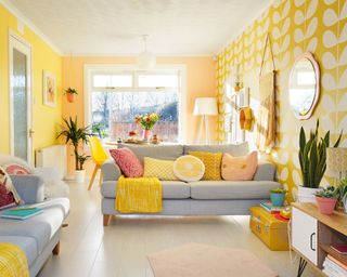 Playful yellow and gray living room with yellow wall paint, retro patterned wallpaper, and light gray sofas styled with assorted novelty throw pillows.
