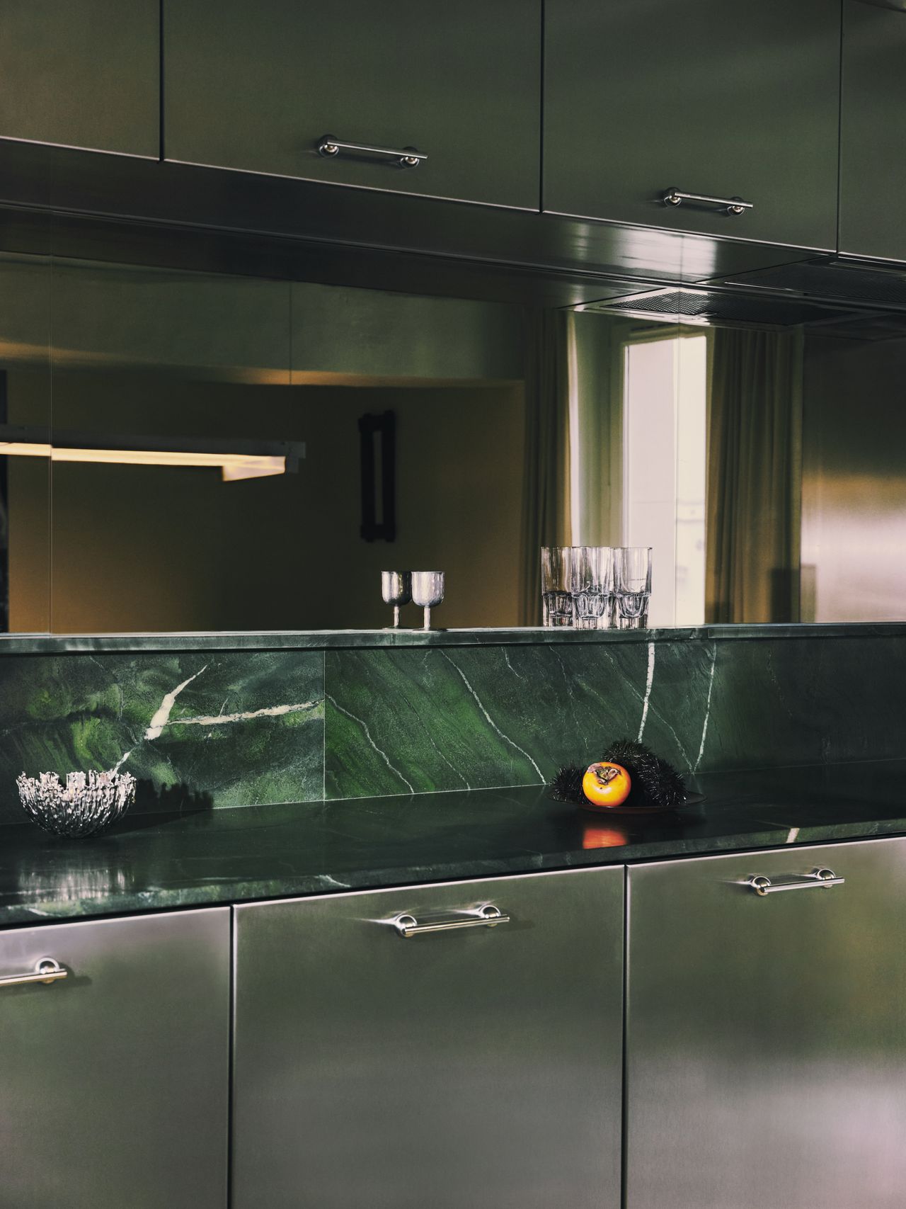 A sleekly designed apartment with tiled white and black checkered floors, chrome surfaces, brick walls, and occasional pops of red, ming green, and butter across linearly cut furniture.