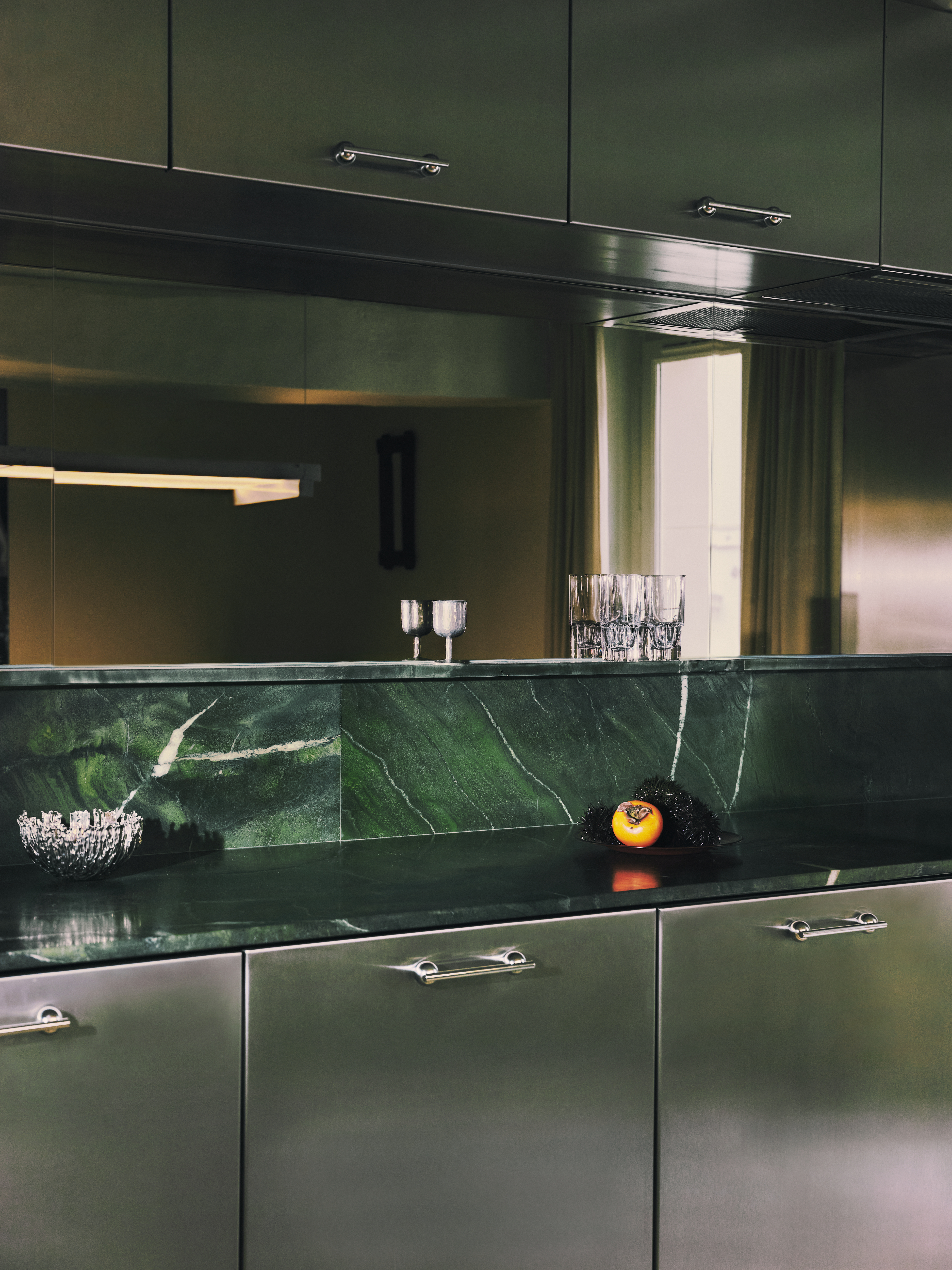 A sleekly designed apartment with tiled white and black checkered floors, chrome surfaces, brick walls, and occasional pops of red, ming green, and butter across linearly cut furniture.