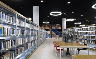 Bookshelves in the Birmingham library with wooden tables and chairs and circular ceiling lights