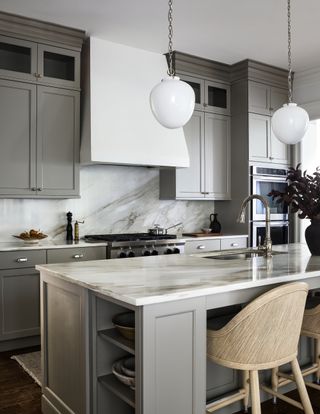 A kitchen with light grey cabinetry and a marble island