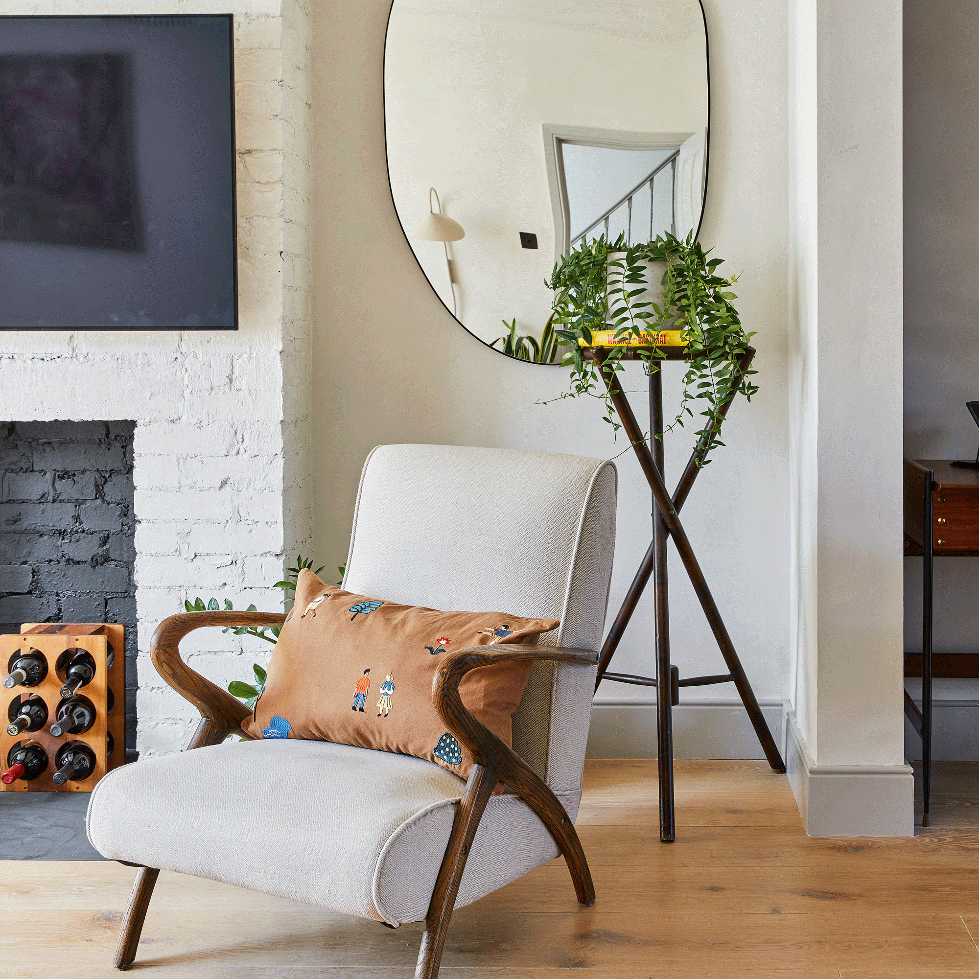 a living room with a mid century vintage armchair with a large mirror on the wall and a tripod plant stand