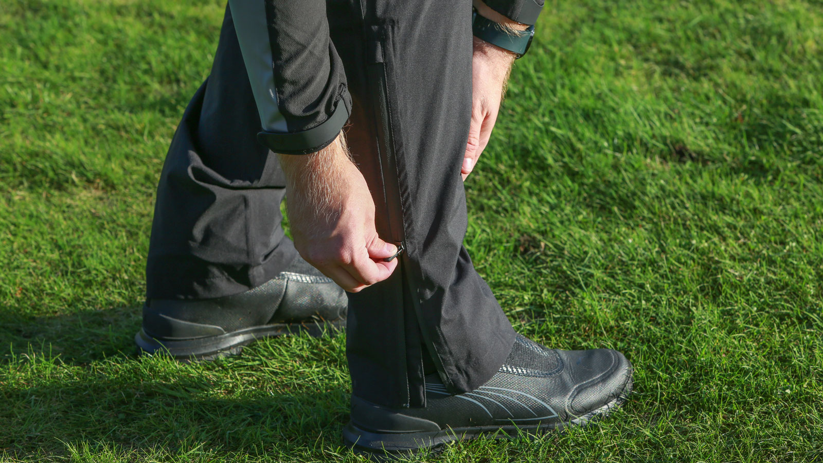 A golfer adjusts the leg of the Puma DRYLBL Rain Waterproof Golf Pants