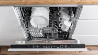 An open dishwasher door, with dinner plates, side plates and mugs inside
