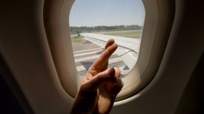 Fingers crossed in front of an airplane window that looks out on a runway.