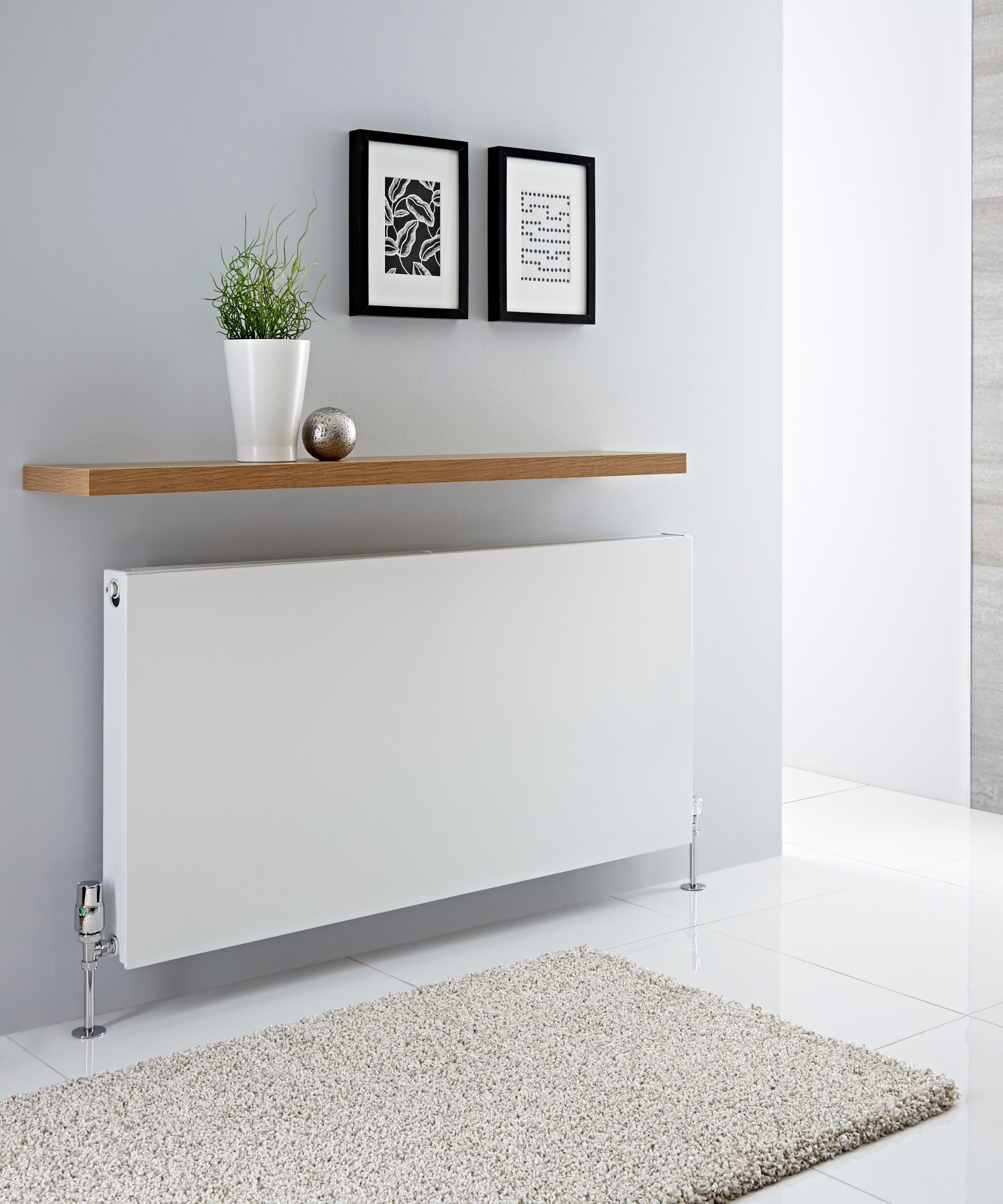 A simple floating oak shelf above a slimline white radiator creates extra display space while keeping the look clean and minimal.