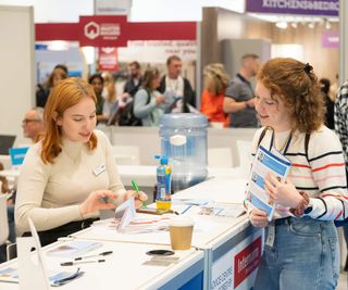 Ask the experts desk at the Homebuilding & Renovating Show, showing a member of team advising a member of the public on appointment times