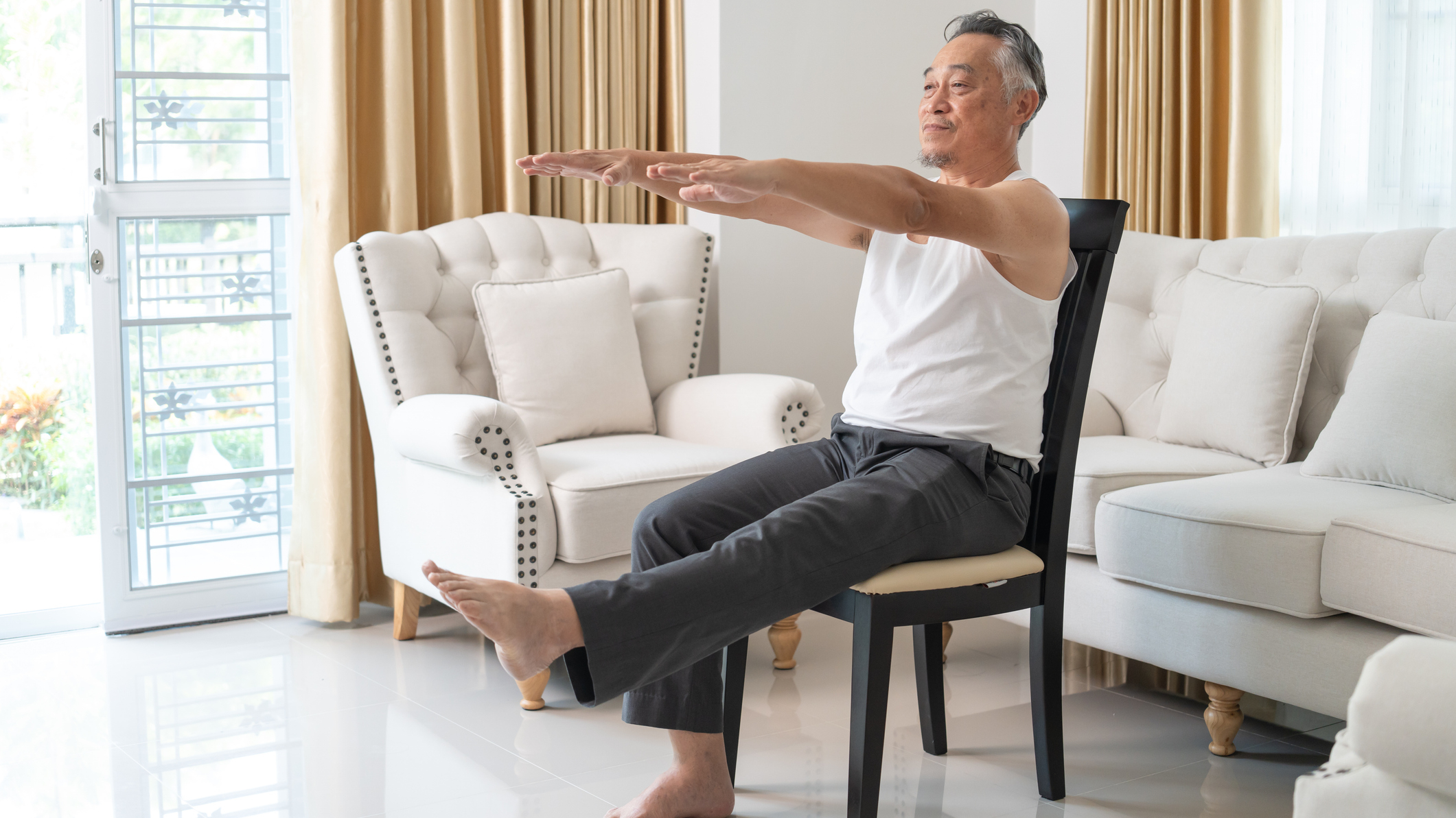 Man sits in chair in domestic setting with his arms and one leg extended in front of him