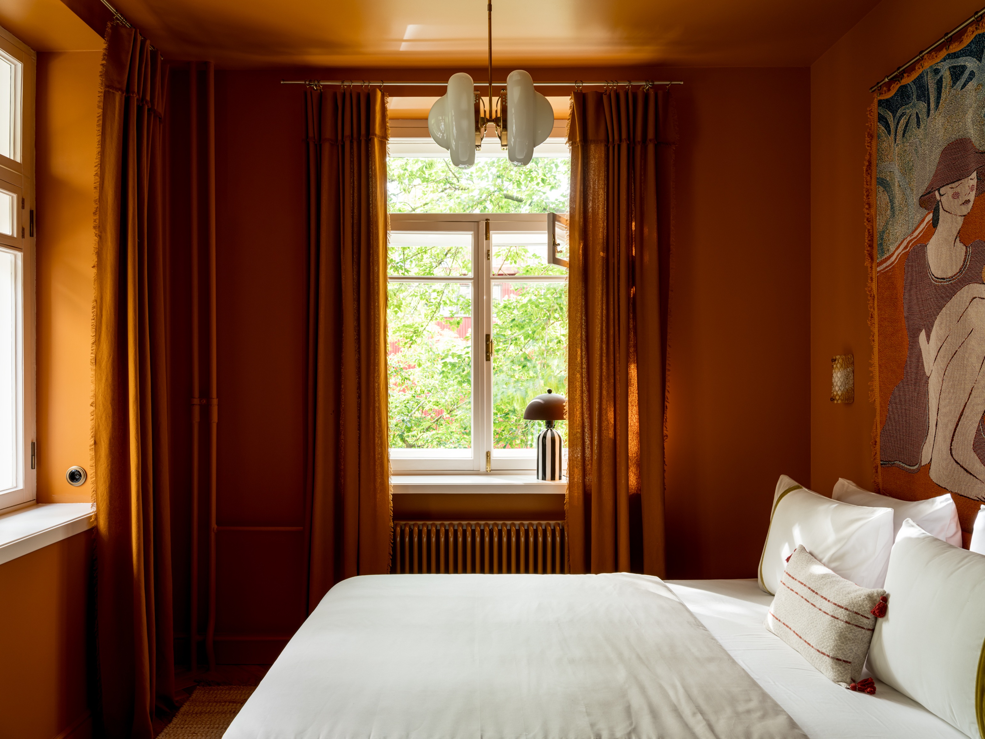 an orange color drenched bedroom with orange curtains and a tapestry on the wall