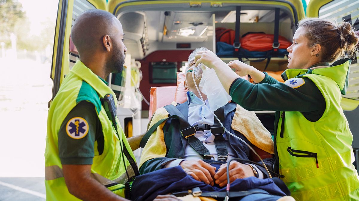 Male and female paramedics treat a man outside an ambulance