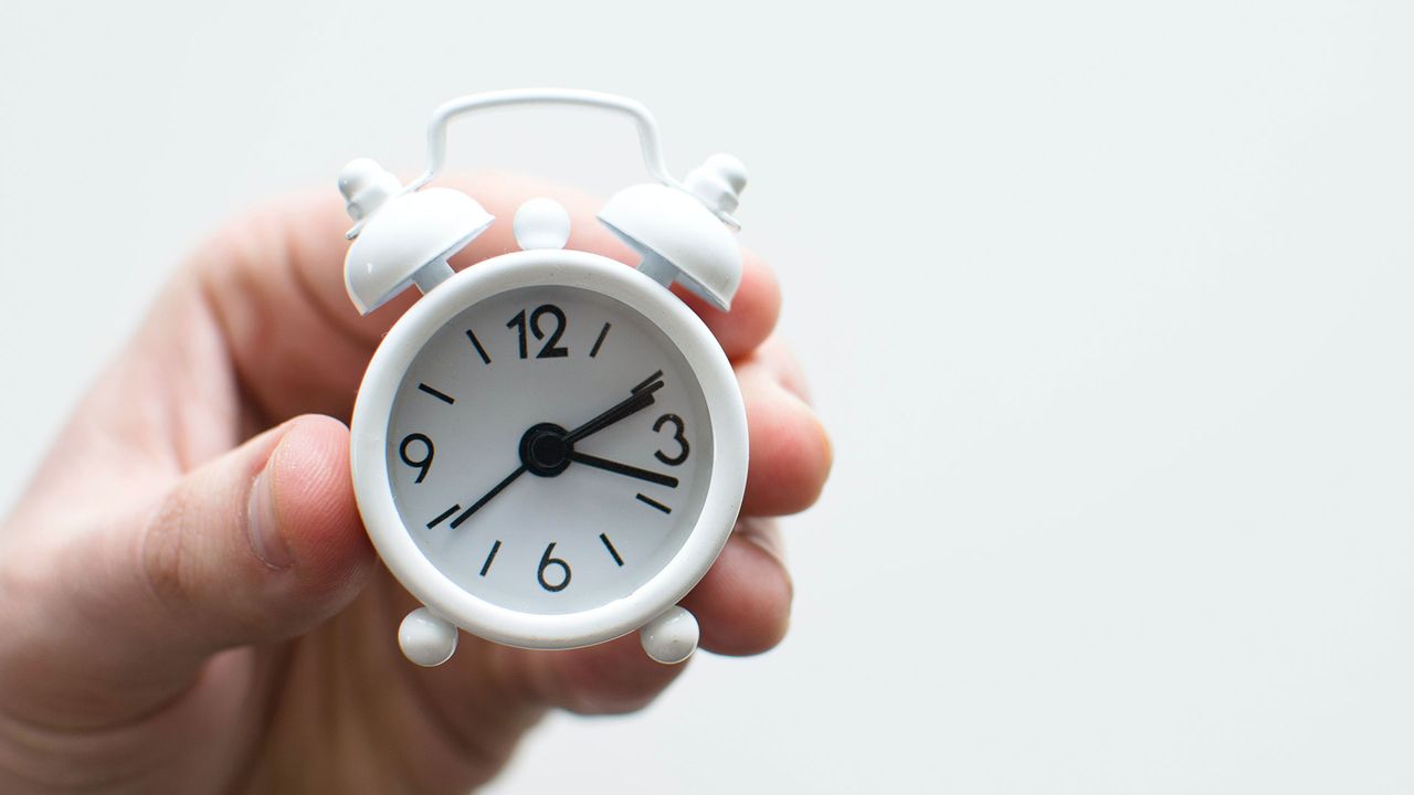 Hand holding tiny alarm clock