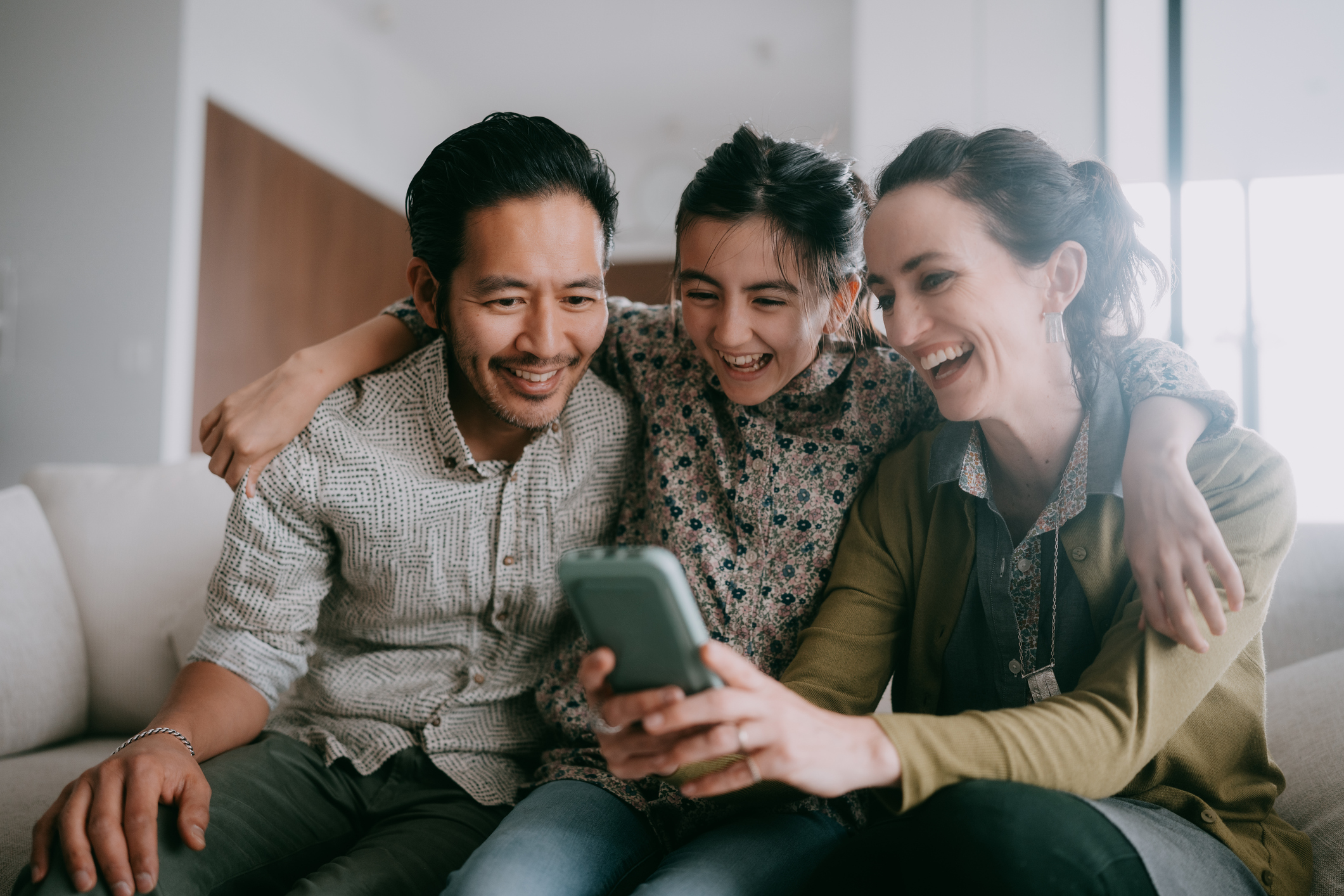 Three people sitting together, smiling at a smartphone.