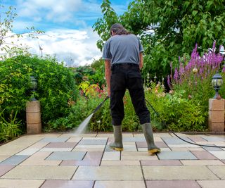 A person cleaning a paved patio in a mix of paving colours using a pressure washer