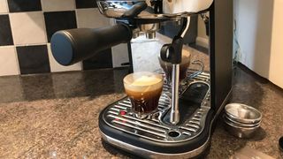 En Breville Bambino Plus står i hörnet på en köksbänk med en färdigbryggt espresso.