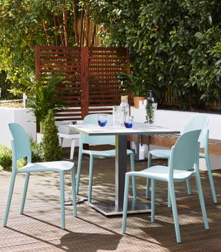 easy to clean blue Danetti outdoor dining set on a wooden deck with a fence and planted boundaries in the background