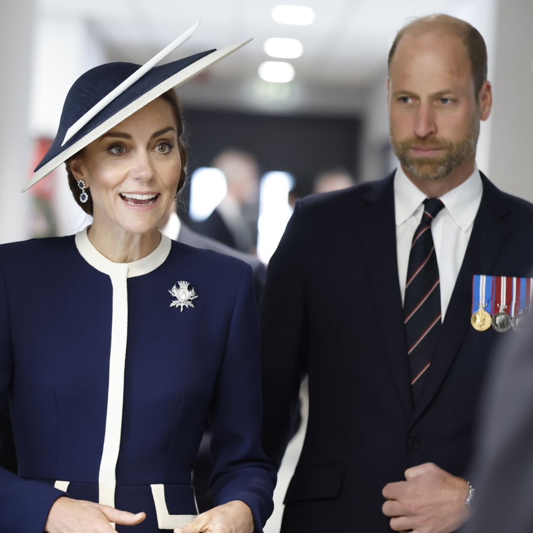Kate Middleton wears a navy dress with white accents and a matching hat while Prince William wears a suit with medals