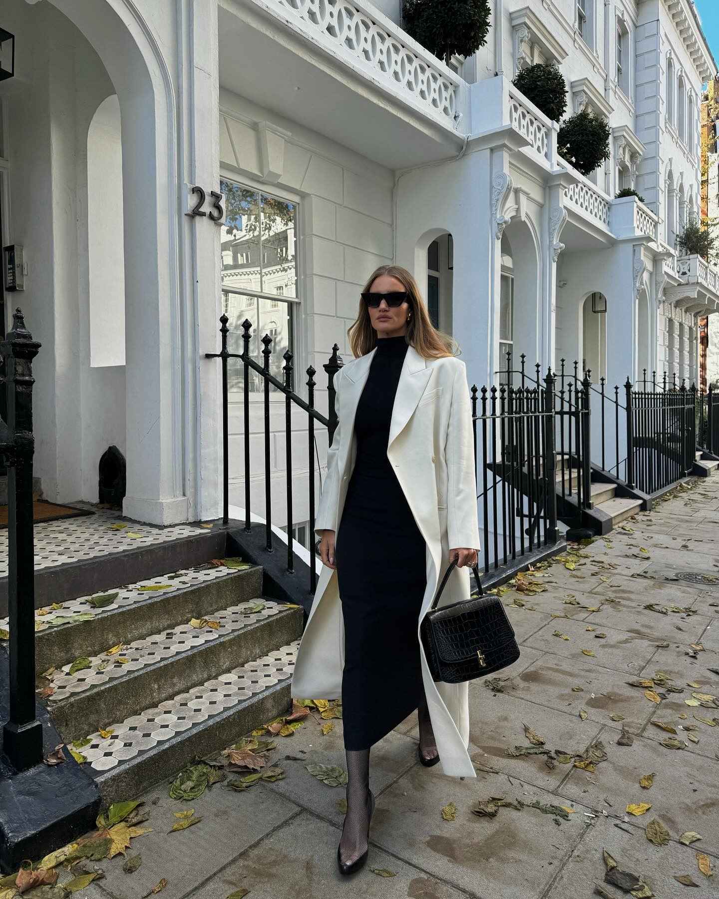 Rosie Huntington-Whiteley wears a white coat, black dress and carries The Row Torba bag