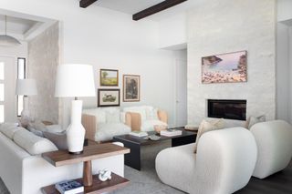 living room with white walls, boucle and sheepskin chairs, beams on ceiling and stone fireplace wall
