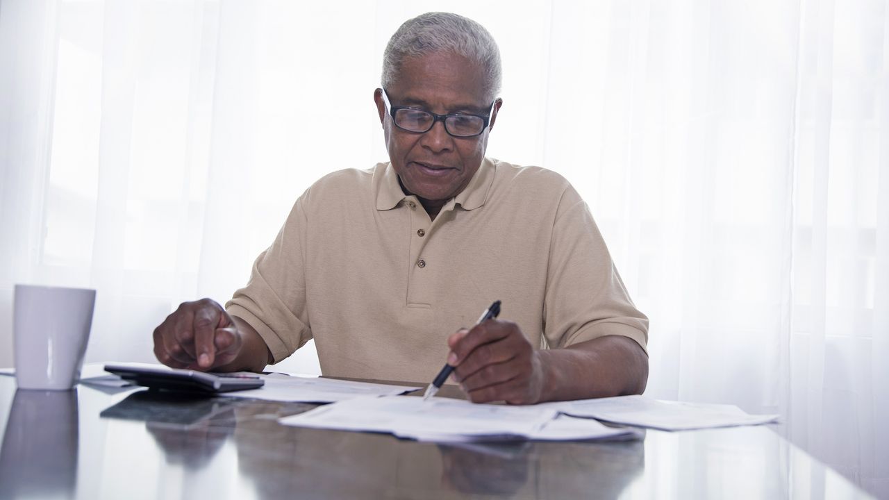 A man uses a calculator as he goes over paperwork at the kitchen table.