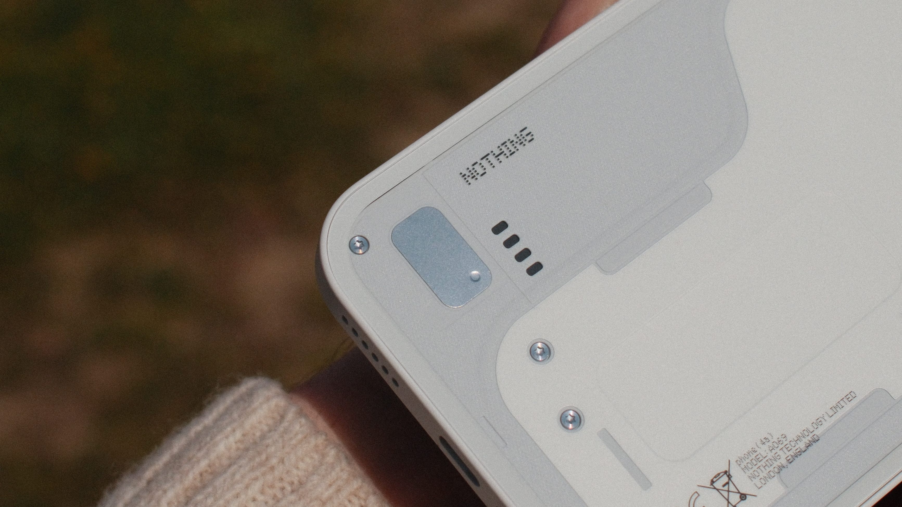 Close-up of the lower rear section of the Nothing Phone (4a) showing the speaker grille, branding and design screws.
