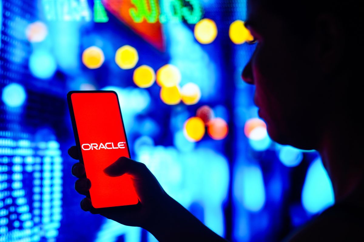 Somebody holding a smartphone showing the Oracle logo against a colourful backdrop