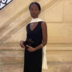 Influencer @sylviemus_ wears a black v-neck dress with black pointed-toe slingbacks and a white scarf.