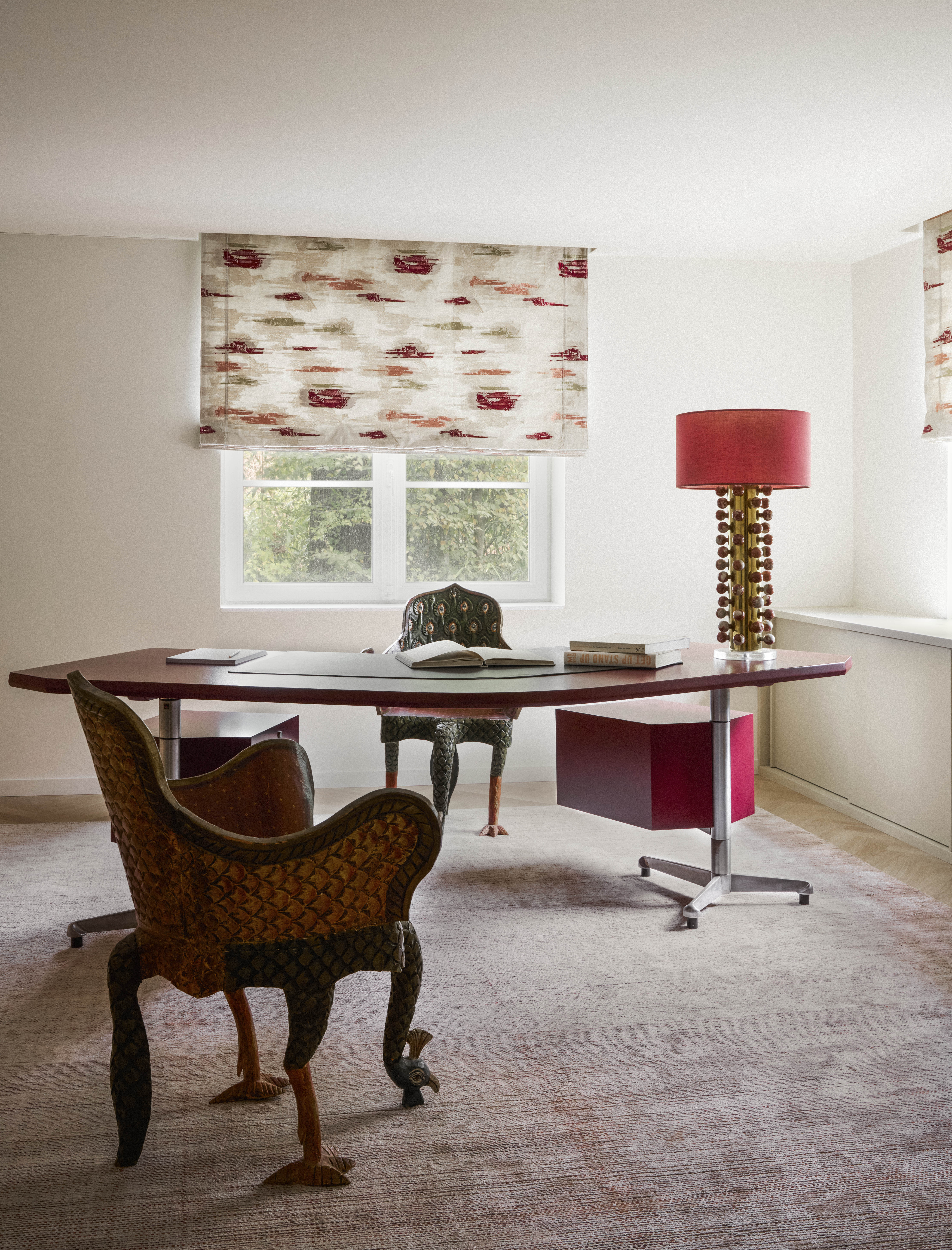 A home office with vintage chairs, a red lamp, a sculptural table and otherwise muted palette