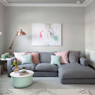grey living room with a abstract painting above a grey sofa with colorful pillows and a white top with a turquoise base coffee table
