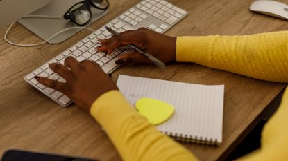 A woman has a notepad in front of her while working on her computer.