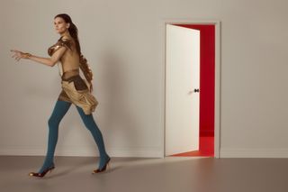 Model in colourful, eclectic outfit walks through a door to a red room wearing looks from the S/S 2025 season