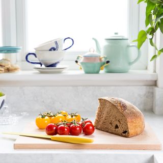 Kitchen makeover, close up of fresh bread and yellow and red tomatoes on the vine on wooden cutting board on composite worktop