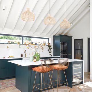 kitchen extension with white walls and ceiling navy blue cabinetry with island, two bar stools and wine fridge