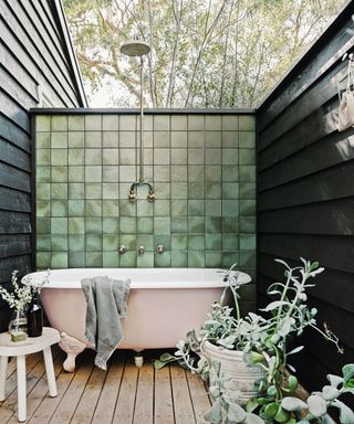 Outdoor bathroom with pink bathtub against green tiled wall