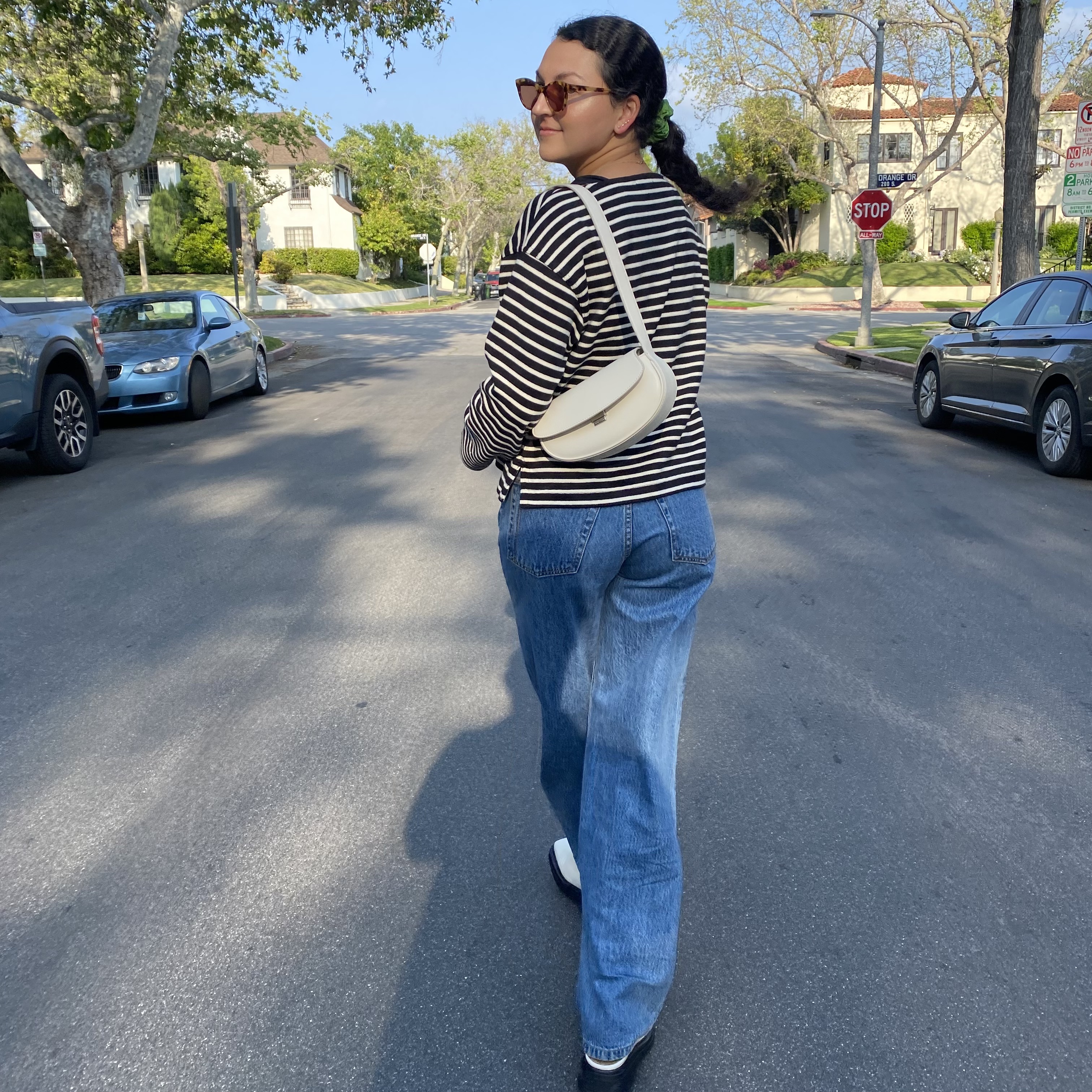Woman in a striped shirt, jeans, white shoes, and a cream handbag.