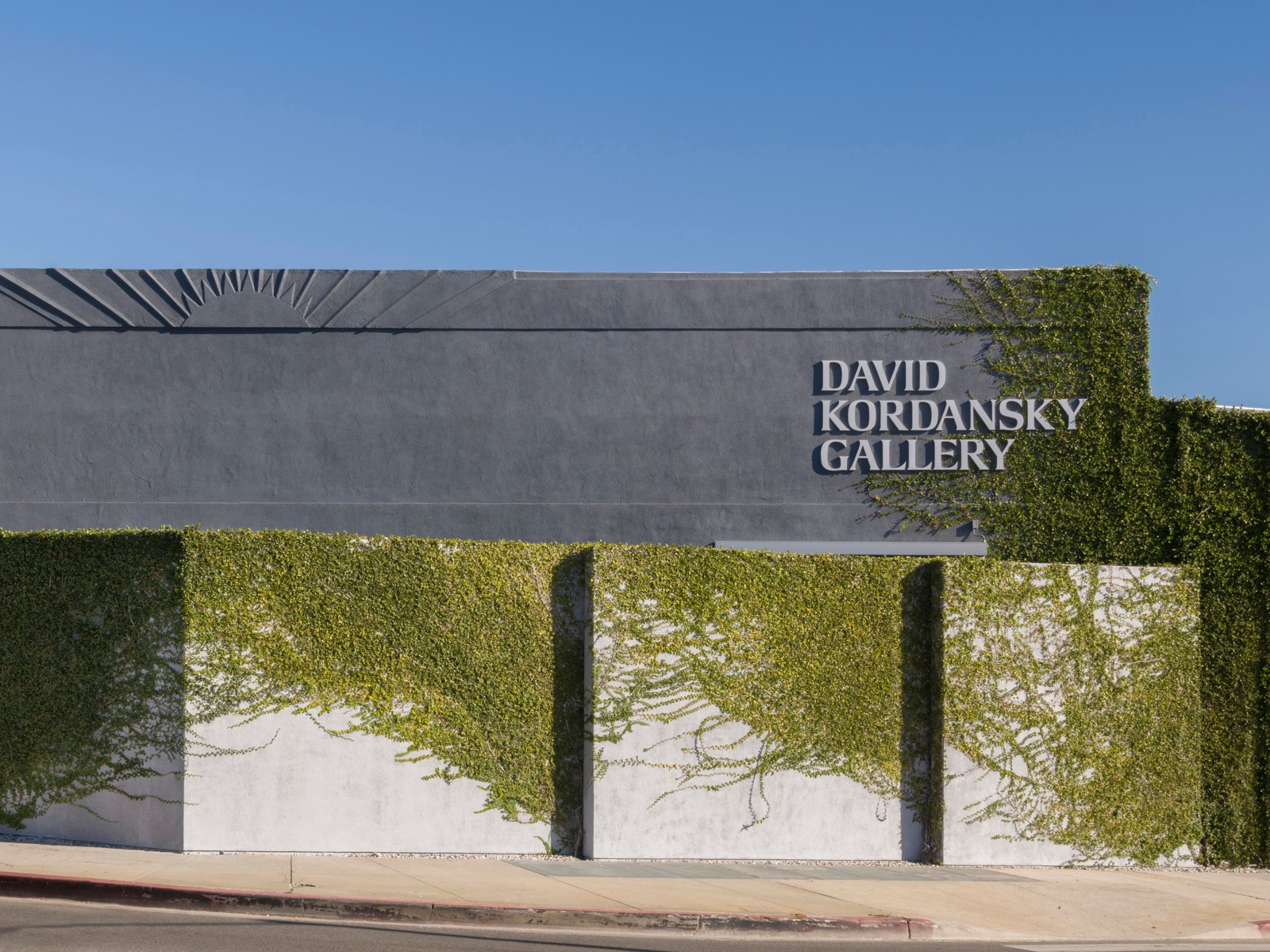 The brutalist exteriors of a gallery boasts cement walls revived by thriving ivy and a sign that reads "DAVID KORDANSKY GALLERY" in capital grey letters.