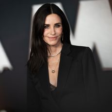 a white woman with dark hair posing for paparazzi in front of a black and white background