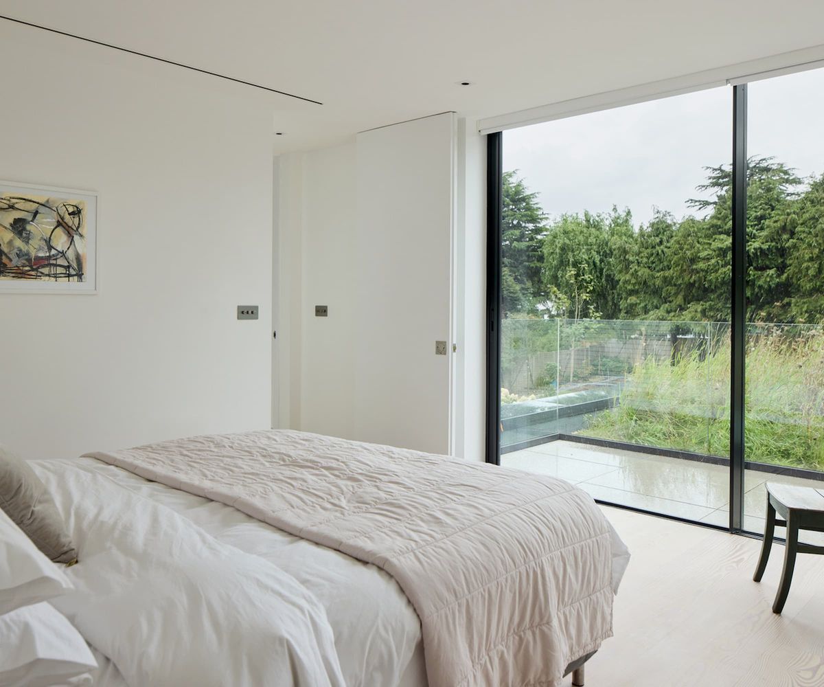 A white bedroom with bifold doors leading to a balcony overlooking a green roof