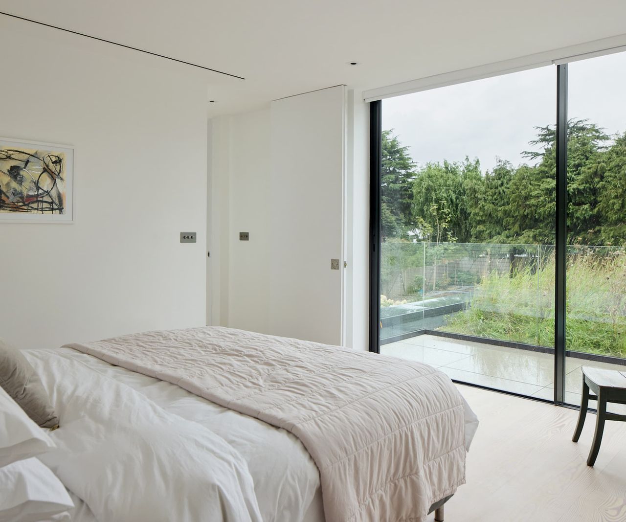 A white bedroom with bifold doors leading to a balcony overlooking a green roof