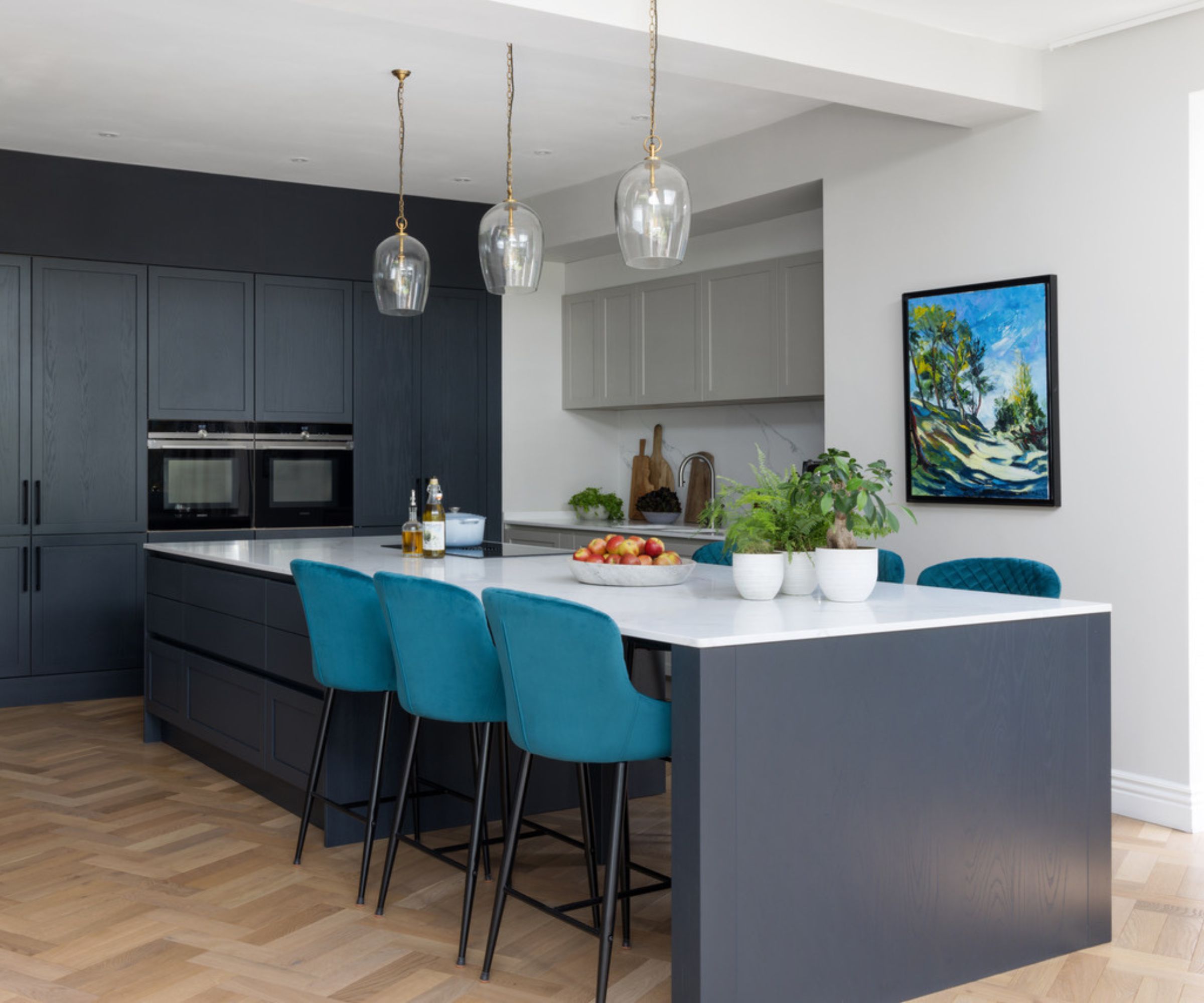 A large kitchen with dark blue cabinets and island, white marble countertops, and wooden parquet flooring