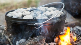 A dutch oven sitting in the campfire covered in hot coals