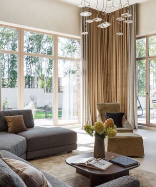 Bright living room with large windows, sofa, chair, wooden coffee table with flowers and statement light fixture