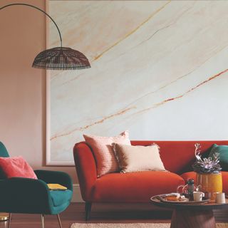 A pink-painted living room with a red sofa and a teal velvet armchair