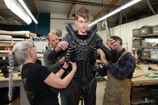 a tall man is getting dressed as an alien monster with three assistants